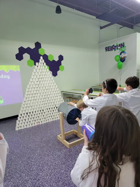 Kids in lab coats doing hands-on science experiments at Reaction Lab